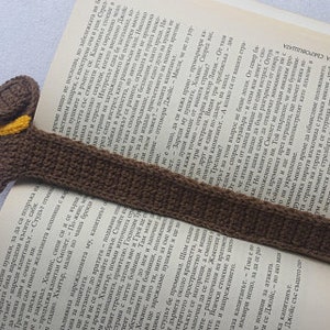 Peut inclure: Marque-page fait main en crochet en forme de chien teckel marron avec un collier jaune. Le corps du chien s'&eacute;tend le long de la page du livre ouvert, servant de marque-page. Un accessoire de lecture artisanal.