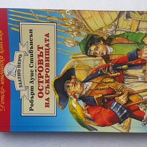 Peut inclure: Un marque-page en crochet marron en forme de souris est ins&eacute;r&eacute; dans un livre intitul&eacute; "L'&Icirc;le au tr&eacute;sor" de Robert Louis Stevenson. La couverture du livre pr&eacute;sente une illustration color&eacute;e de pirates.