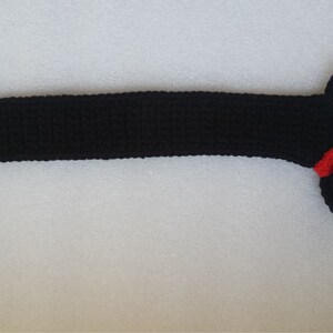 Peut inclure: Un chien teckel noir au crochet avec un collier rouge. Le chien a un long corps et de courtes pattes. La t&ecirc;te pr&eacute;sente un &oelig;il blanc et un nez noir. Fait &agrave; la main.