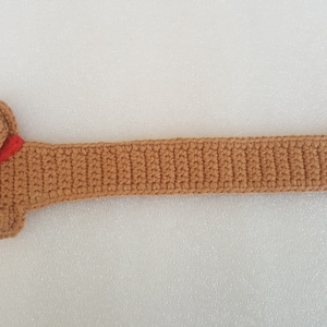 Peut inclure: Un chien teckel au crochet marron avec un collier rouge. Le chien a un long corps et de courtes pattes, et une petite queue. Le travail au crochet est d&eacute;taill&eacute;, montrant la texture du fil. Le chien mesure environ 50 cm de long.