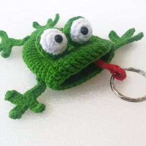 K&ouml;nnte beinhalten: Gr&uuml;ner geh&auml;kelter Frosch-Schl&uuml;sselanh&auml;nger mit gro&szlig;en wei&szlig;en Augen und einer herausgestreckten roten Zunge. Der Frosch h&auml;lt einen silbernen Schl&uuml;sselring.