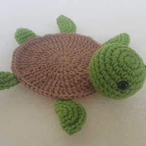 May include: A handmade crochet turtle in shades of brown and green. The turtle has a brown shell, green head, and four green flippers. The eyes are small black beads. This soft toy is perfect for children.