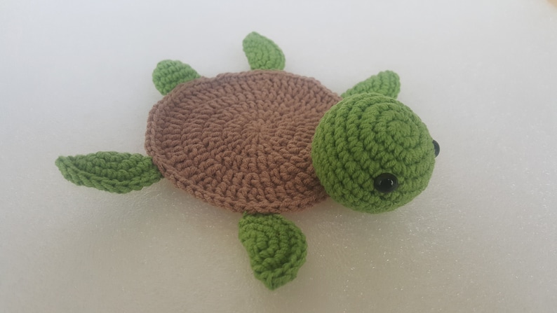 May include: A handmade crochet turtle in shades of brown and green. The turtle has a brown shell, green head, and four green flippers. The eyes are small black beads. This soft toy is perfect for children.