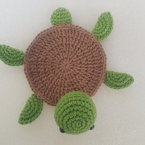 May include: A handmade crochet turtle in shades of brown and green. The turtle has a round brown shell, green flippers, a green head, and small black eyes. This soft toy is perfect for a child's room or as a decorative item.