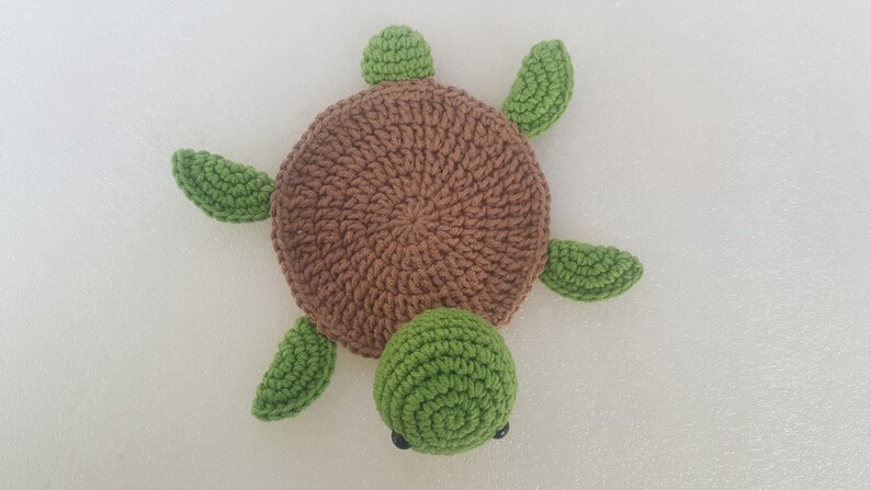 May include: A handmade crochet turtle in shades of brown and green. The turtle has a round brown shell, green flippers, a green head, and small black eyes. This soft toy is perfect for a child's room or as a decorative item.