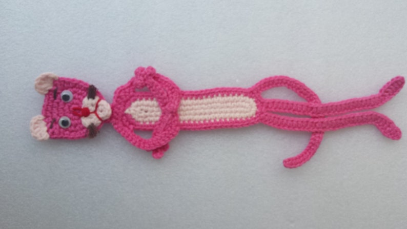 May include: Pink crocheted bookmark shaped like the Pink Panther cartoon character. The bookmark has a white crocheted section in the middle.