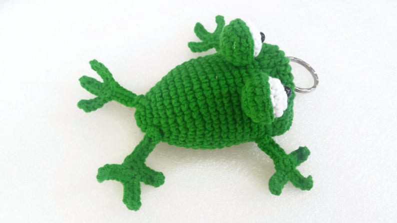 K&ouml;nnte beinhalten: Gr&uuml;ner geh&auml;kelter Frosch-Schl&uuml;sselanh&auml;nger mit wei&szlig;en Augen und einem silbernen Schl&uuml;sselring.