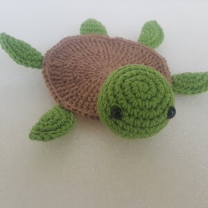May include: A handmade crochet turtle toy. The turtle has a brown shell, a green head, and green flippers. The eyes are small black beads. The toy is made of soft yarn.