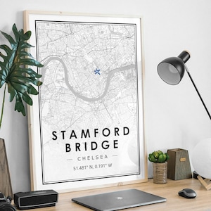 Puede incluir: Una impresión de mapa en blanco y negro de Stamford Bridge en Chelsea, Londres, con una estrella azul que marca la ubicación. La impresión está enmarcada en un marco de madera clara y tiene el texto "Stamford Bridge - Chelsea - 51.481° N, 0.191° W" impreso debajo del mapa.