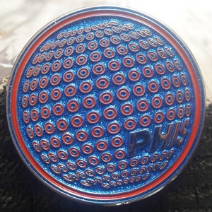 May include: A blue and red circular pin with a textured surface and the text "PHIS" in white letters.
