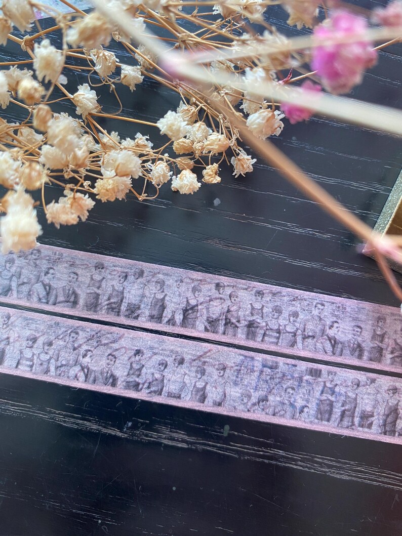 May include: Two rolls of decorative washi tape with a vintage design featuring a group of people in black and white. The tape is on a dark wood surface.