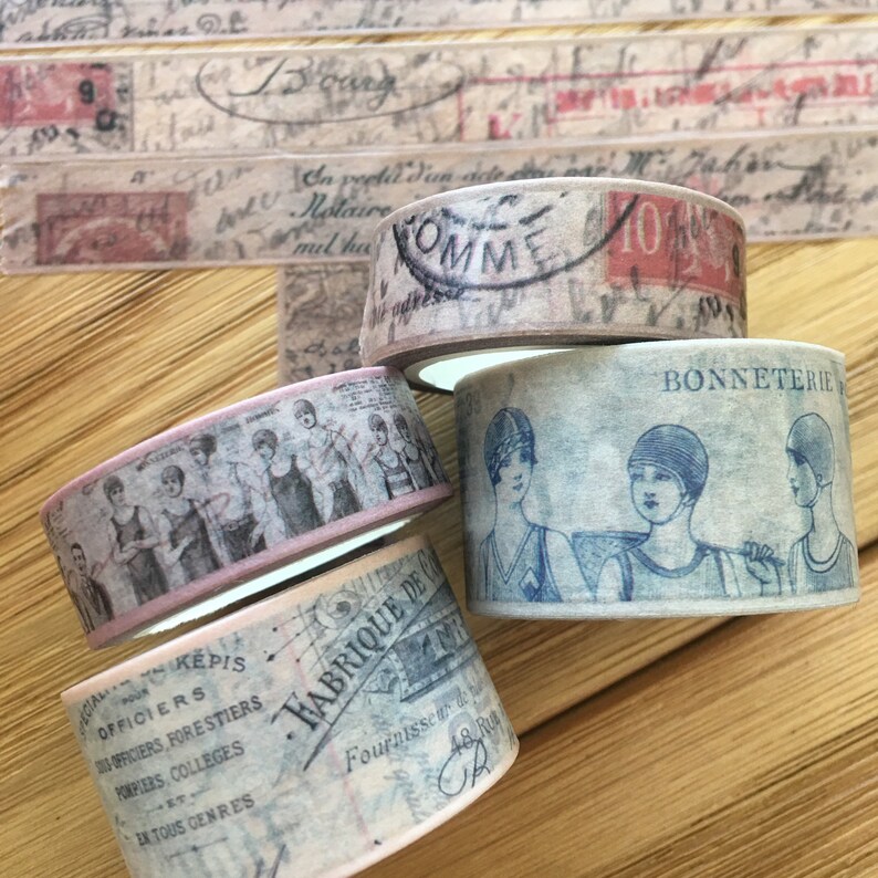 May include: Four rolls of vintage-style washi tape with different designs. The designs include a group of women in vintage swimsuits, a French text pattern, a stamp with the word "SOMME", and a pattern with the text "BONNETERIE".