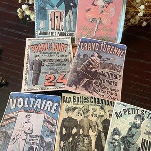 Puede incluir: Postales publicitarias vintage que muestran tiendas de ropa en Par&iacute;s, Francia. Las postales presentan ilustraciones de hombres y mujeres con ropa, junto con texto en franc&eacute;s. Las postales est&aacute;n impresas en papel grueso y tienen un aspecto desgastado y antiguo.