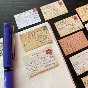 May include: A collection of vintage postcards with handwritten messages and stamps. The postcards are on a lined notebook page with a blue pen.
