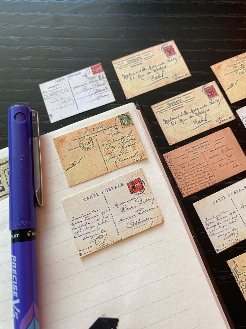 May include: A collection of vintage postcards with handwritten messages and stamps. The postcards are on a lined notebook page with a blue pen.