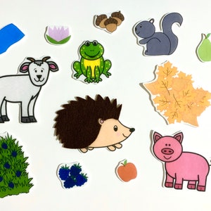 May include: A set of colorful felt animal and nature cutouts, including a goat, frog, hedgehog, squirrel, pig, leaves, berries, a pear, a lotus flower, acorns, and a blue rectangle.