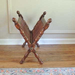 May include: A wooden magazine rack with a criss-cross design and a brass knob. The rack is made of dark brown wood and has a rustic look.