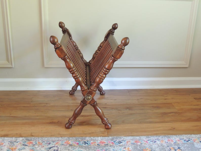 May include: A wooden magazine rack with a criss-cross design and a brass knob. The rack is made of dark brown wood and has a rustic look.