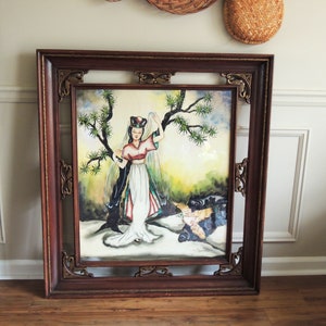 May include: A framed painting of a woman in a white dress with a red and blue sash, standing in a forest setting. The painting is in a dark wood frame with gold accents.