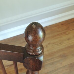 May include: A close-up of a wooden stair banister with a dark brown finish. The banister has a decorative finial on top.