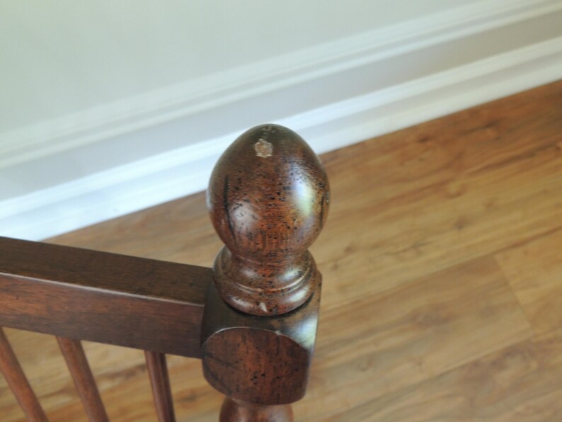 May include: A close-up of a wooden stair banister with a dark brown finish. The banister has a decorative finial on top.