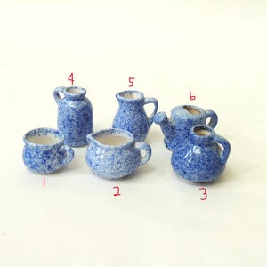 Könnte beinhalten: Eine Sammlung von sechs Miniatur-Keramikteilen in Blau und Weiß. Das Set umfasst eine kleine Tasse, zwei Krüge, eine kleine Vase, eine Teekanne und einen größeren Krug. Die Teile haben ein gesprenkeltes Design und sind auf einer weißen Oberfläche angeordnet.