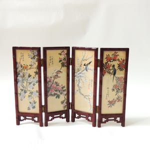 May include: A small, four-panel folding screen with a dark red wooden frame. Each panel displays a painting of birds and flowering branches in yellow, pink, and blue. The screen is a decorative item, likely for display.