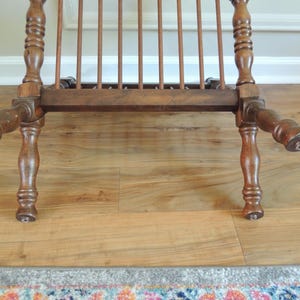 May include: A wooden chair with a slatted back and turned legs. The chair is brown and has a distressed finish.