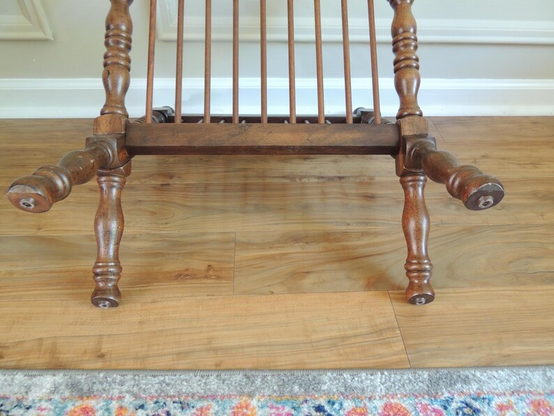 May include: A wooden chair with a slatted back and turned legs. The chair is brown and has a distressed finish.