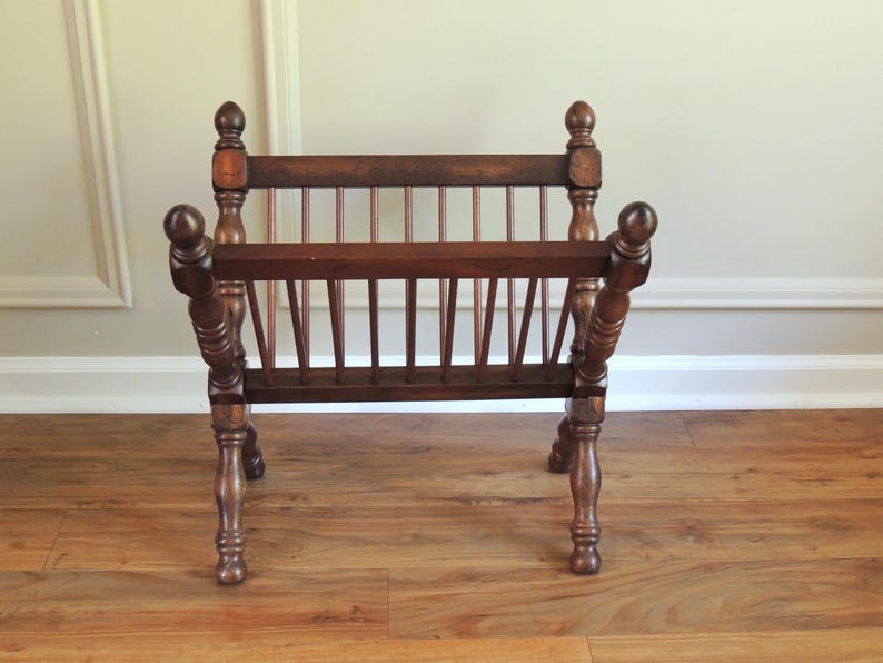 May include: A wooden magazine rack with a slatted design and turned legs. The rack is made of dark brown wood and has a rustic look.