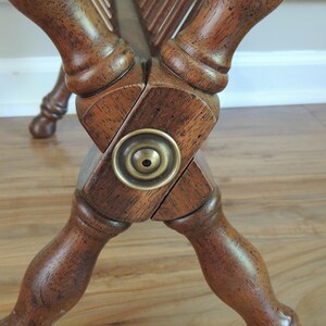May include: Close-up of the wooden base of a magazine rack with a brass accent. The base is made of dark wood and has a cross-shaped design. The brass accent is a round knob with a small hole in the center.