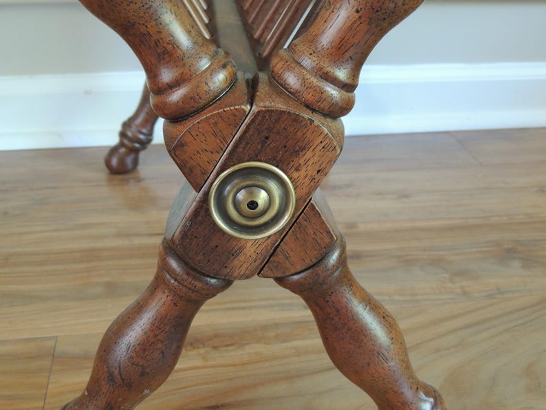 May include: Close-up of the wooden base of a magazine rack with a brass accent. The base is made of dark wood and has a cross-shaped design. The brass accent is a round knob with a small hole in the center.