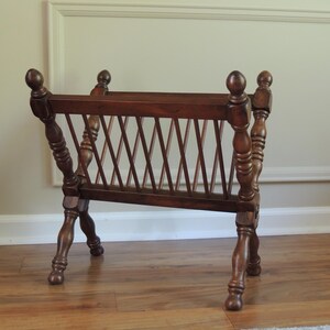 May include: A wooden magazine rack with a criss-cross design on the front. The rack has four legs that are crossed at the bottom.