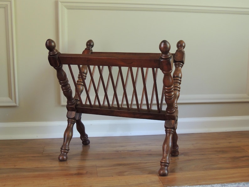 May include: A wooden magazine rack with a criss-cross design on the front. The rack has four legs that are crossed at the bottom.