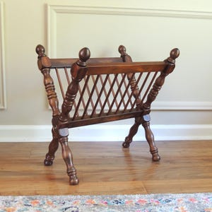May include: A wooden magazine rack with a criss-cross design and turned legs.