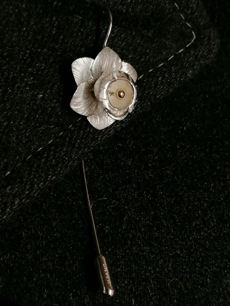 Puede incluir: Broche de narciso de plata con un centro dorado. La broche est&aacute; unida a un alfiler de plata.
