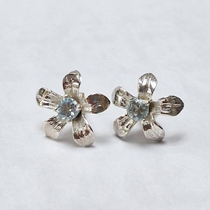 May include: A pair of silver flower-shaped earrings with light blue gemstones in the center.