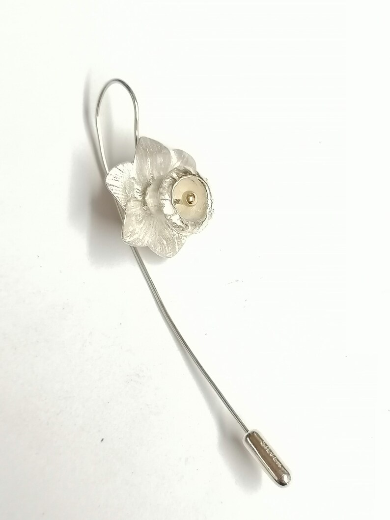 Puede incluir: Broche de narciso de plata con un centro dorado. La broche tiene un alfiler largo y delgado.