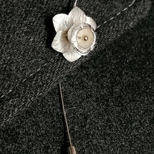 Puede incluir: Un broche de plata en forma de narciso con un centro dorado. El broche est&aacute; unido a un alfiler de plata.
