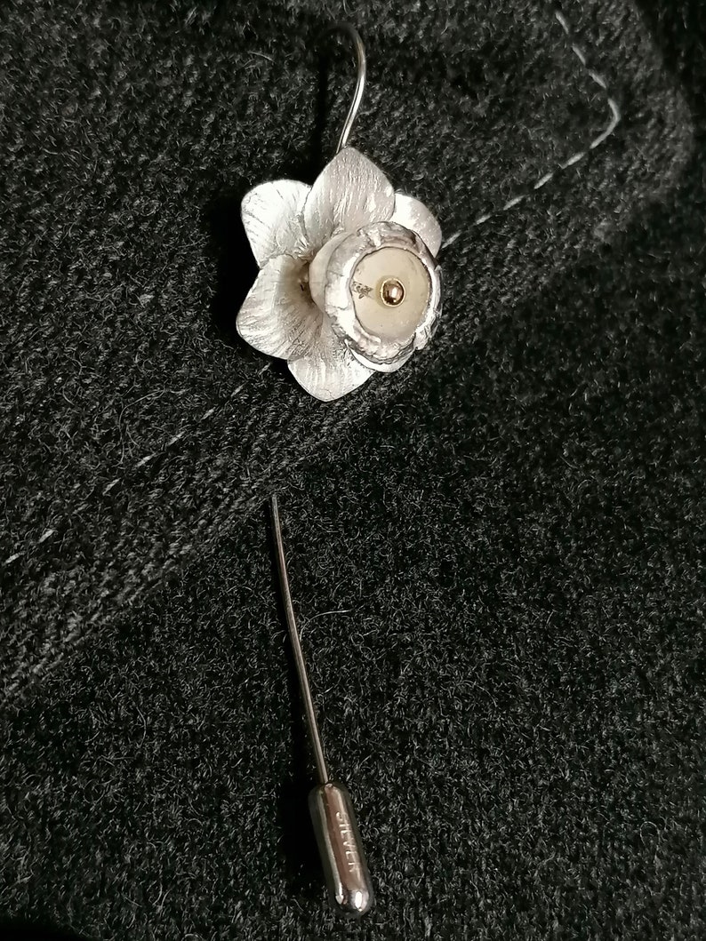 Puede incluir: Un broche de plata en forma de narciso con un centro dorado. El broche est&aacute; unido a un alfiler de plata.
