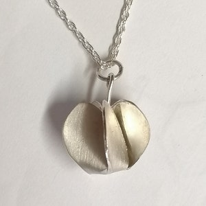 May include: A silver necklace with a geometric pendant. The pendant is made of multiple pieces of silver that are folded together to create a unique shape.