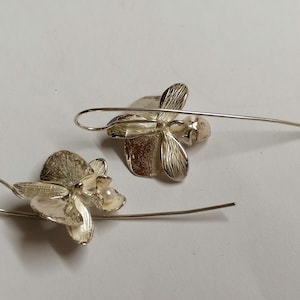May include: A pair of silver orchid earrings with a pearl accent. The earrings are dangle style with a delicate wire.