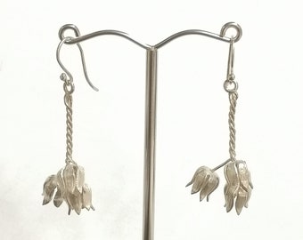 May include: Silver dangle earrings with a flower design. The earrings are hanging from a silver hook.