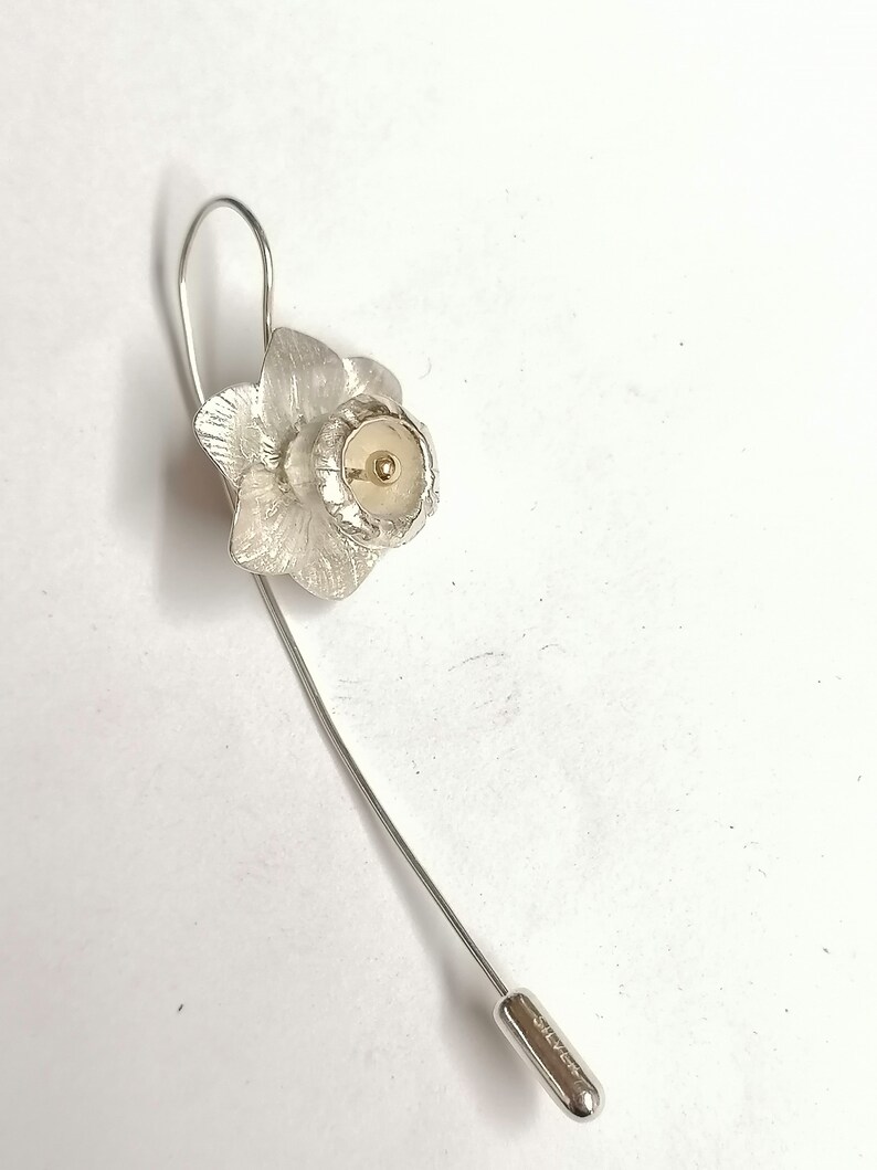 Puede incluir: Broche de narciso de plata con un centro dorado. La broche tiene un alfiler largo con una tapa de plata que dice "Silver."