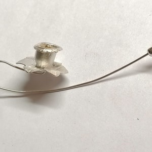 Puede incluir: Un broche de plata con forma de flor con un centro dorado. El broche est&aacute; unido a un alfiler de plata.