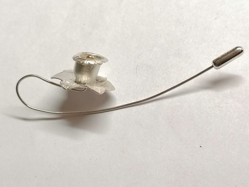 Puede incluir: Un broche de plata con forma de flor con un centro dorado. El broche est&aacute; unido a un alfiler de plata.