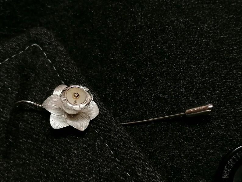 Puede incluir: Un broche de flor de plata con un centro dorado. El broche est&aacute; unido a un alfiler de plata.