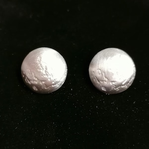 Op de afbeelding: Een paar zilverkleurige oorbellen met een getextureerd, licht bobbelig oppervlak.