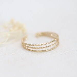 Könnte beinhalten: Ein goldfarbener Ring mit drei Bändern aus strukturiertem Metall. Jedes Band besteht aus kleinen, runden Perlen.