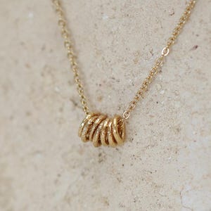 Peut inclure: Un collier en chaîne dorée avec un pendentif composé de plusieurs anneaux dorés empilés.